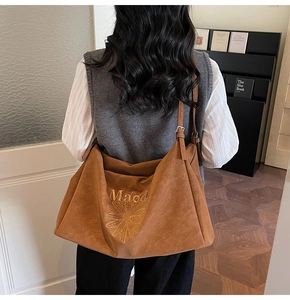 Rear view of model wearing a large brown suede hobo bag with floral embroidery detail