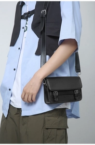 Detail of matte black leather messenger bag with silver buckles on crossbody strap