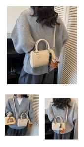 Detail of cream Boston bag featuring embossed logo, bear charm and checkered ribbon