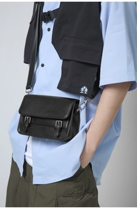 Detail of a black matte leather messenger bag featuring dual silver buckles and adjustable strap