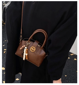 Brown shell-shaped bag with wooden bead charm worn over a classic black coat