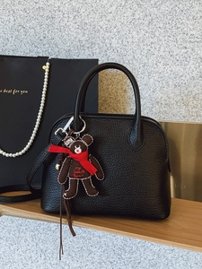 Elegant black lychee leather shell bag with bear charm on a light wooden surface