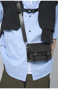 Detail of black crossbody bag with flap dual-buckle design and wide shoulder strap on model