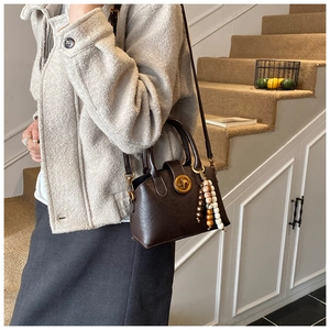 Detail of dark brown shell bag with golden rotary lock and boho beaded charm decoration