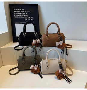Detailed view of suede-like Boston bags in black, coffee, green, and beige with bear charms