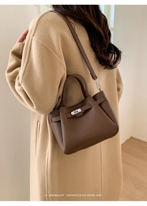 Détail du sac seau en cuir marron grainé porté en bandoulière sur un manteau d'hiver beige