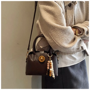 Side view of vintage brown shell bag with golden rotary lock and beaded pendant detail