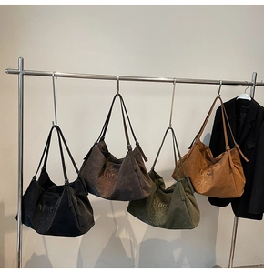 Detail showing four embroidered tote bags in black, green, and brown on a garment rack