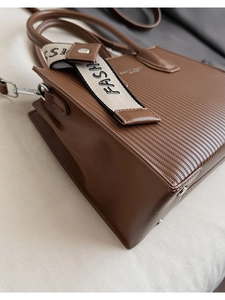 Macro detail of brown tote bag featuring vertical striped embossing and fashion ribbon