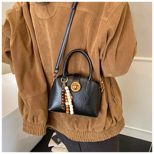 Detail of black leather shell bag with gold round lock and wooden bead tassel accessory