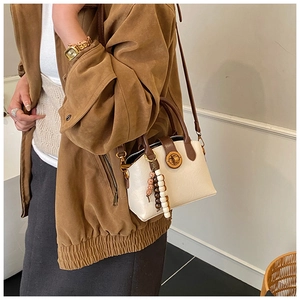 Cream shell bag with brown trim and colorful bead charm worn on suede jacket