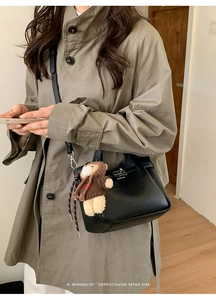 Détail du sac seau noir motif litchi avec pendentif ours sur un long manteau beige