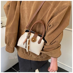 Detail of vintage cream crossbody bag featuring a golden lock and elegant bead charm
