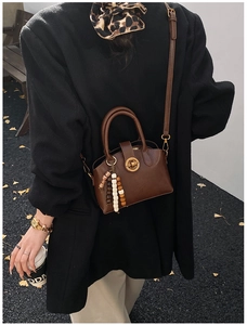 Detail of brown vintage leather crossbody bag with metal lock and beaded charm accessory