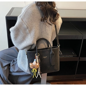 Detailed view of black leather bucket bag with a cute plush bear charm on a grey sweater