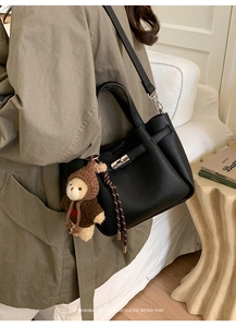 Détail d'un sac seau en cuir noir grainé avec boucle argentée et breloque ourson