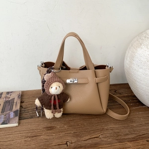 Gros plan du sac seau en cuir grainé kaki avec fermoir en métal et breloque ours