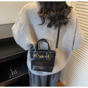 Detail of vintage black leather bucket bag with gold clasp and adjustable strap on model