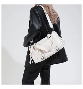 Model wearing a white leather tote bag with metal rings and tassel detail over a black suit