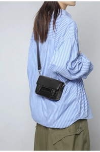 Detail view of the black leather mini crossbody bag showing straps and metal buckles