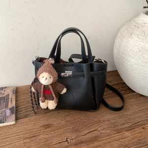 Détail d'un sac seau en cuir grainé noir avec un charm d'ours brun sur une table en bois