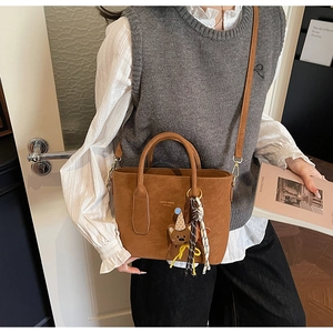Brown suede bucket bag detail with teddy bear charm and polka dot scarf on a model