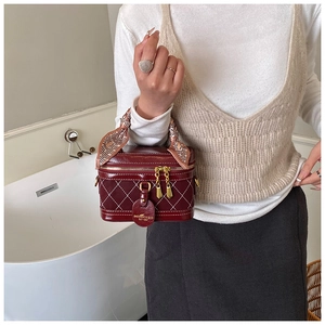 Detail of burgundy quilted box bag with silk scarf handle and gold zipper hardware