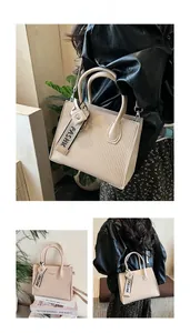 Detailed macro view of the beige textured square bag with fashion logo ribbon and handles