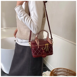 Detail of burgundy quilted box bag featuring a silk scarf handle and gold hardware