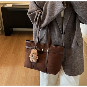 Detail of dark brown suede tote bag featuring side leather straps and gold buckle accents