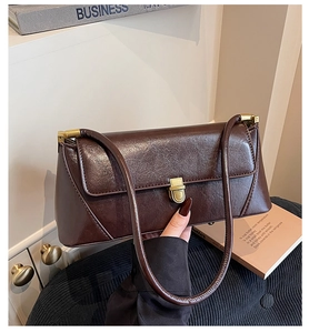 Detail of a dark brown glossy leather baguette bag featuring a gold metal buckle