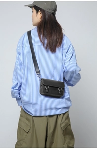 Detail of black crossbody bag with double buckle straps worn with casual outfit