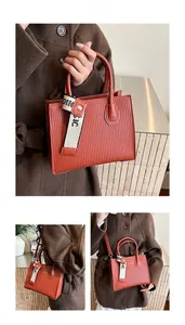 Close-up of orange pleated small square bag with letter ribbon and metal rivet detail