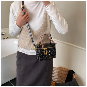 Detail of a black quilted crossbody box bag with chain strap and decorative silk scarf
