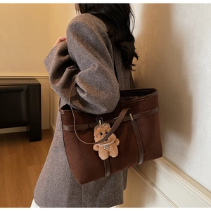 Close-up of retro suede tote bag texture with brown leather strap and cute bear charm