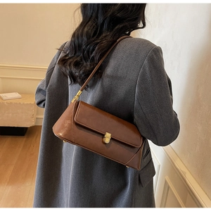 Detail of a brown leather baguette bag with a golden clasp on a textured gray blazer
