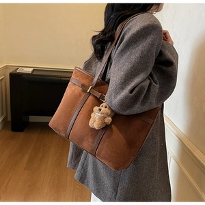 Detail of vintage brown suede tote bag with leather straps and plush bear charm