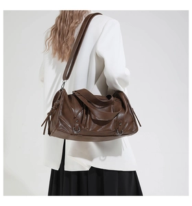 Detail of dark brown leather pillow bag featuring side tassels and a metallic ring buckle