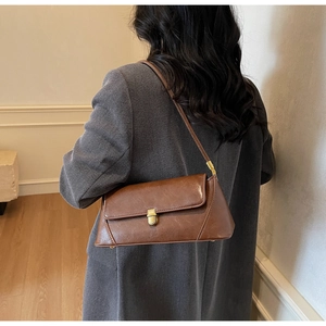 Detail of a brown rectangular baguette bag with a gold metal clasp on a gray suit jacket