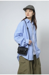 Model wearing a black leather crossbody messenger bag with double buckle flap design