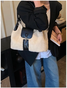 Detail of cream plush shoulder bag with black leather trim worn by a model in a cozy setting
