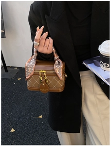 Detail of brown quilted leather handbag with decorative silk scarf handle in street setting