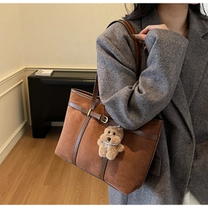 Detail view of large brown suede tote bag with leather trim and plush puppy charm