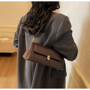 Detail of dark brown baguette bag with gold twist lock worn by model in gray coat