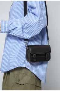 Close-up of minimalist black leather crossbody bag with silver buckles and adjustable strap
