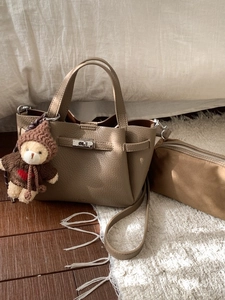 Sac seau en cuir kaki avec breloque ours en peluche sur fond de literie blanche