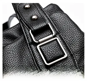 Macro shot of silver metal square buckle and reinforced stitching on black leather tote bag