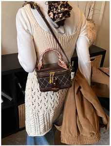Detail of dark brown quilted box bag with a silk scarf handle and golden hardware