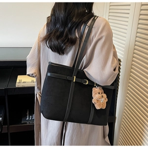 Chic black faux suede tote bag with leather straps and bear charm shown on a model