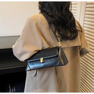 Detail of a chic black glossy shoulder bag with a gold metal twist lock on a beige coat